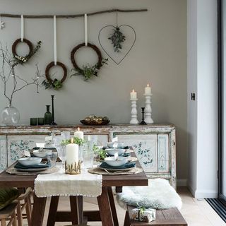 Neutral dining room with wooden table and benches and wreaths on wall
