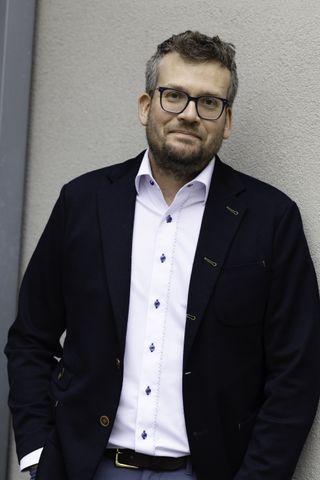 photo of john green wearing black-rimmed glasses, a white shirt and black jacket