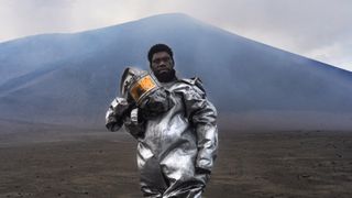 man in protective gear stands at the foot of a volcano