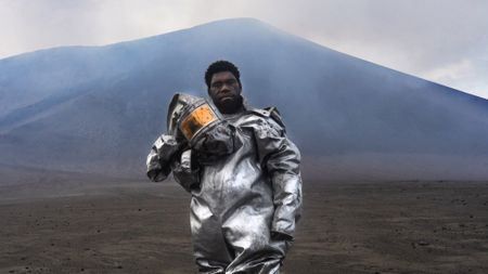 man in protective gear stands at the foot of a volcano