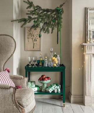 Green drinks trolley with festive foliage hanging above, cozy armchair, artwork on walls
