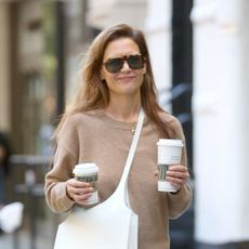 Katie Holmes carries two Starbucks coffees while wearing a camel sweater and plaid skirt in Manhattan