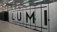 A photo of the Lumi supercomputer in Kajaani, Findland, shot from inside the building. The frame contains the computing cabinets for the supercomputer, which are white and bear the letters "LUMI".