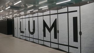 A photo of the Lumi supercomputer in Kajaani, Findland, shot from inside the building. The frame contains the computing cabinets for the supercomputer, which are white and bear the letters &quot;LUMI&quot;.