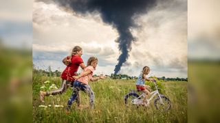 Children playing in Ukraine in the foreground of a burning oil depot from last night's Russian drone strike