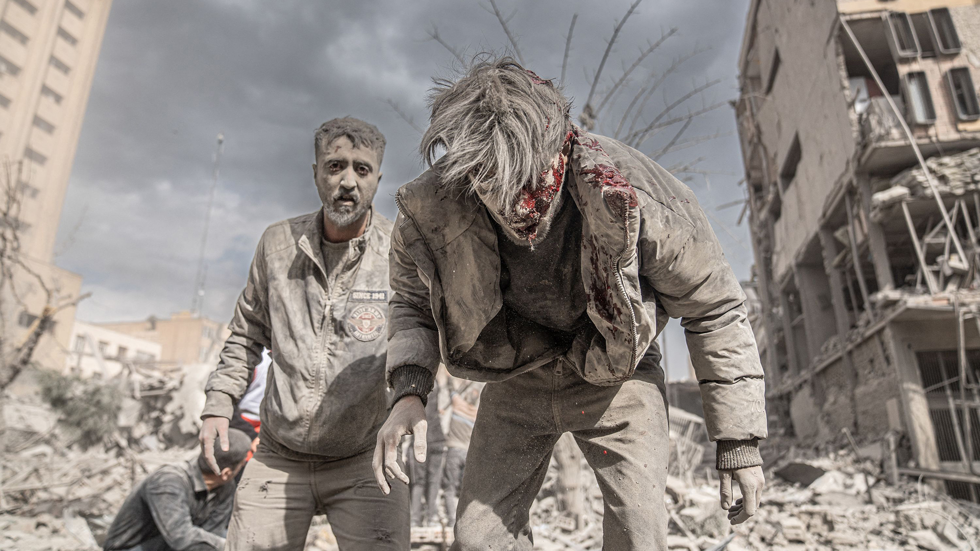 Injured men stumble from the wreckage in the aftermath of a US-Israeli airstrike at Ferdowsi Square in Tehran, Iran