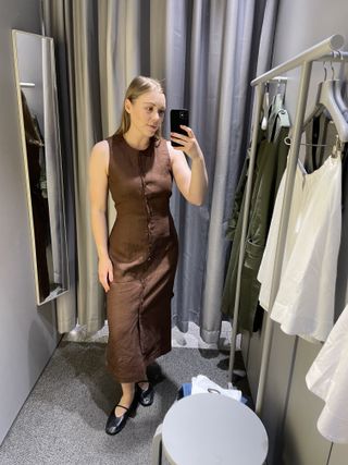 Woman in dressing room wears brown linen dress and black ballet flats