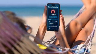 Person relaxing in hammock on beach, looking at home security app on phone