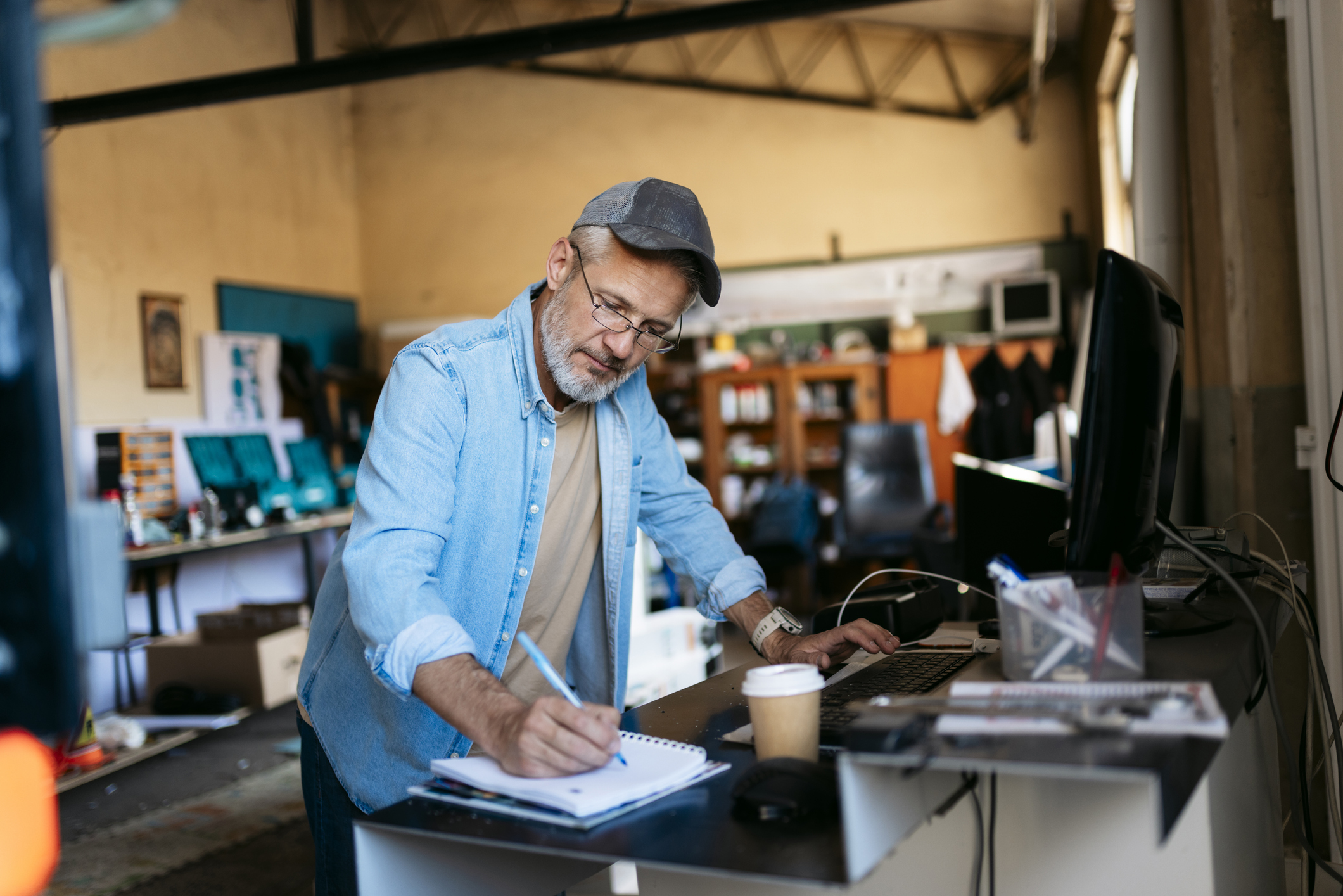 Senior small business owner taking notes and working on a computer in a workshop.