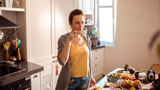 Woman mindfully drinking at home in kitchen, smiling with cup of tea