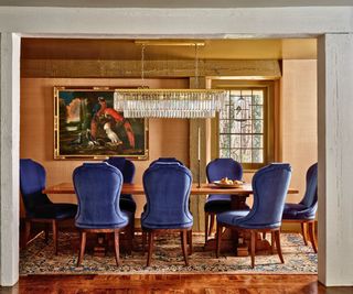dining room with linear chandelier and blue velvet chairs round an antique table
