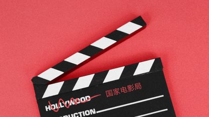 Photo collage of a filmmaker's clapboard on a red background. The word "Hollywood" is scratched out from it, and replaced by the Chinese name of China's Film Administration.