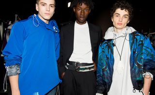 three male models at a fashion week, two wearing blue jackets and one wearing a black blazer