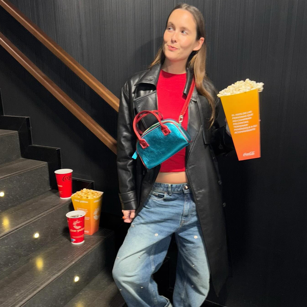 Helena wears a leather jacket, red tee, baggy jeans and a blue bag.