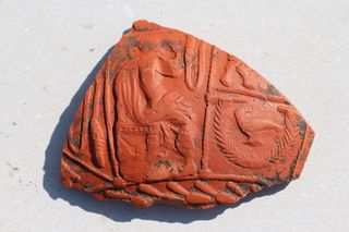 A fragment of a red ceramic shard that shows a detailed relief decoration. This shard and others will help researchers date the site. This piece is dated to about A.D. 100.