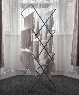 A white heated airer with clothes hanging from it in a bay window