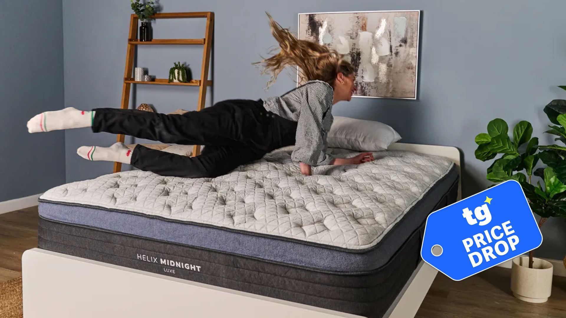 The image shows a light haired mattress tester diving onto the Helix Midnight Luxe mattress, placed on a white bed frame in a neutrally decorated bedroom. Inset, a badge reads 'tg price drop'