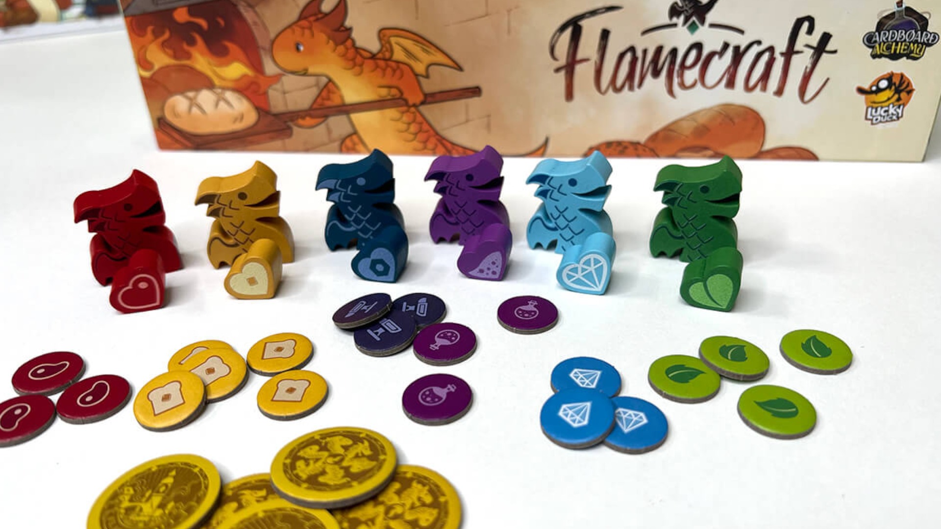 Flamecraft dragon meeples in front of tokens and the box on a white surface