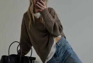 Woman wearing a brown fall sweater with a white tee and jeans.