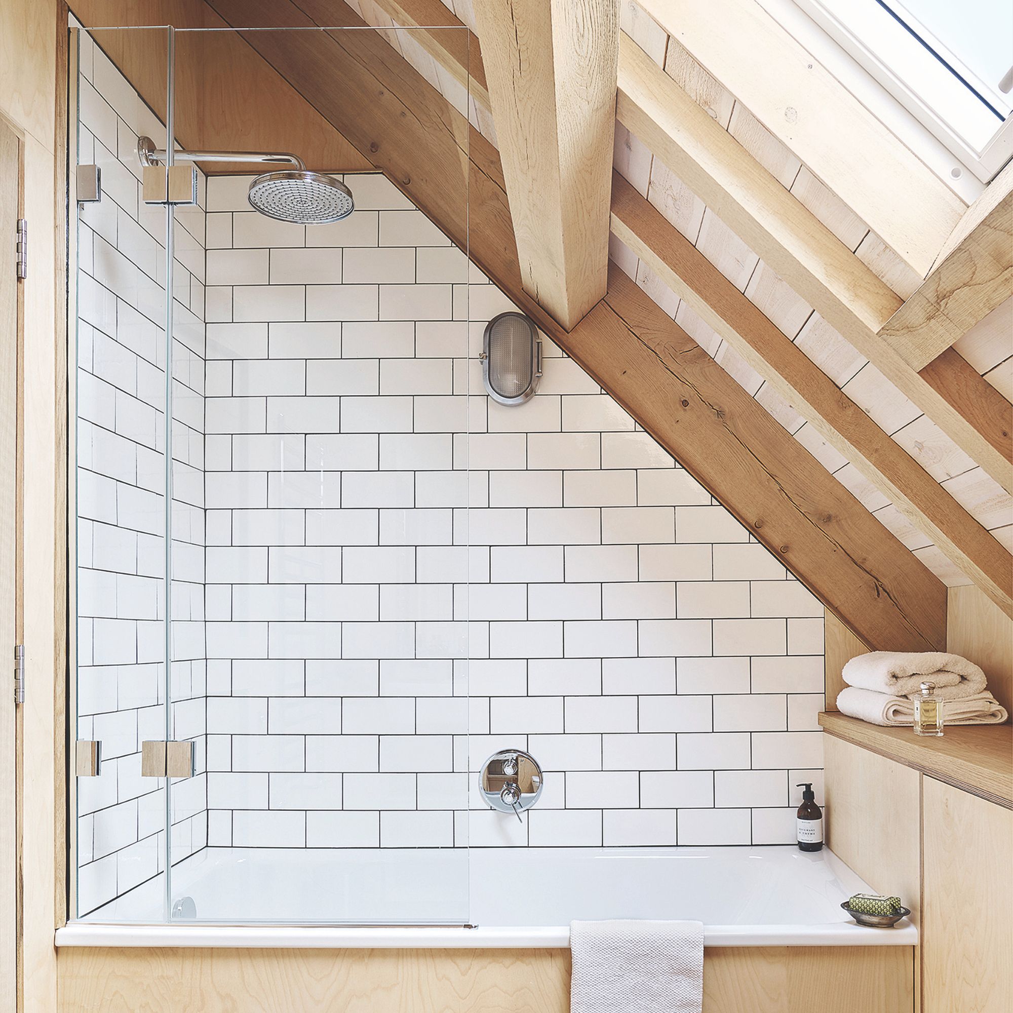 White tiled shower cubicle with wooden surrounds and towels folded on the end