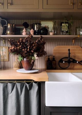 Small laundry room ideas in a brown painted wooden scheme with a jug of dried flowers beside a butler sink.
