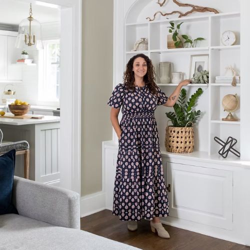 Image of a woman in a printed dress standing next to a white bookshelf