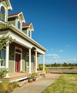 A green painted suburban American home with a lawned front yard, and a view of fields and trees.