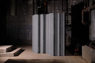 An undulating room divider built from stacked aluminum extrusions that looks like a waste filter. It's set in an industrial factory setting.