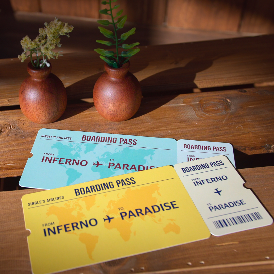 A close-up of a wooden table in a shed, with a wooden barrel in the corner. Yellow and blue boarding passes lay on the table, reading "Single's Airlines. Inferno to Paradise." A promo image from Netflix's 'Single's Inferno' season 5.