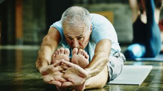 Older man doing yoga stretch at home on floor