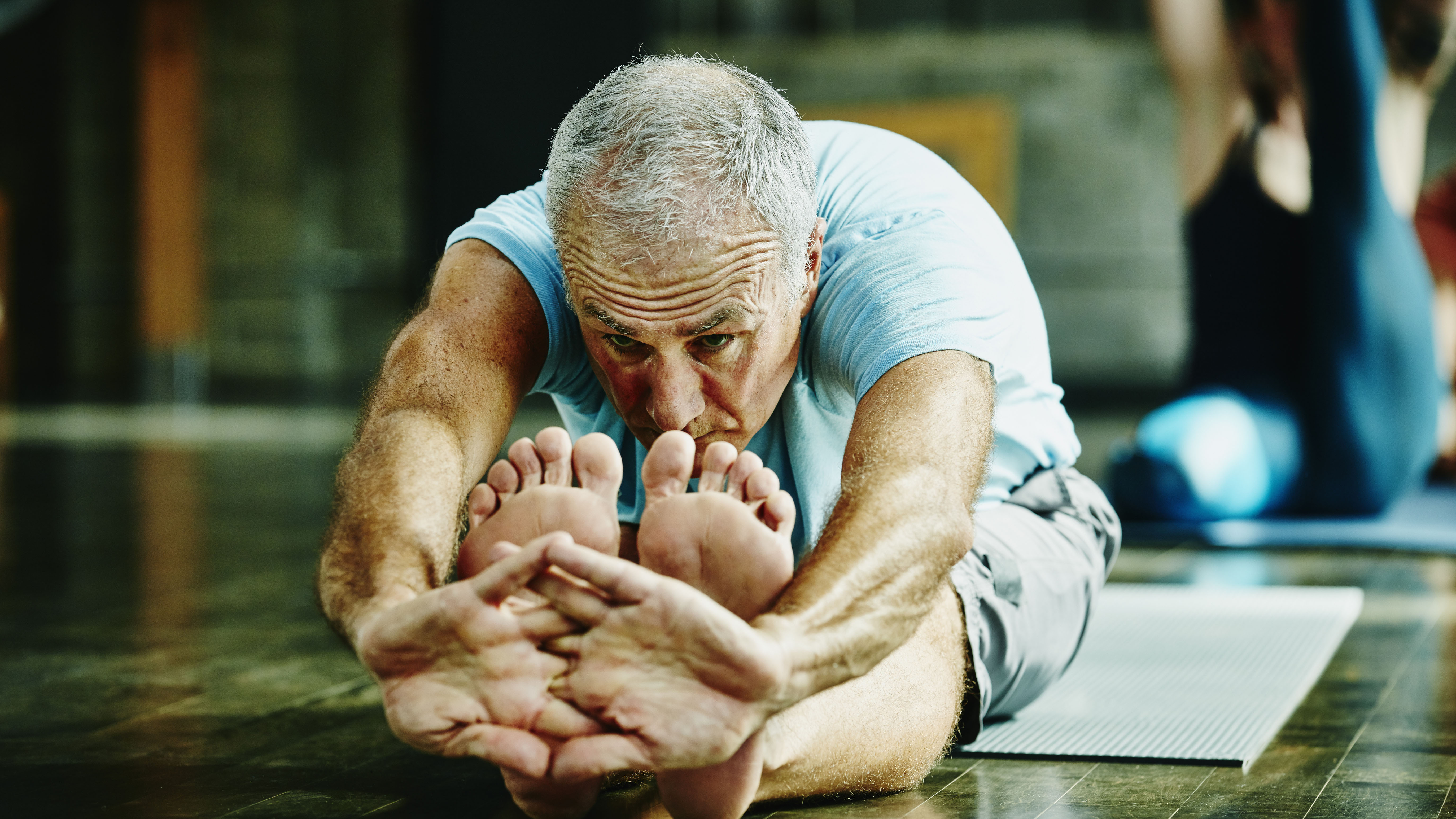 Elderly man doing yoga stretching at home on the floor