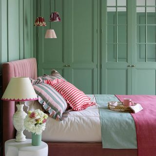 design rules for small bedrooms, green bedroom with paneling, trio of pendant lights, pink and green bedding, table lamp, colourful