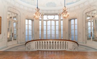 Large windows, two chandeliers hang over a wooden flooring