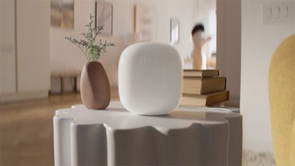 The Nest Wifi Pro sits on a table next to a plant.
