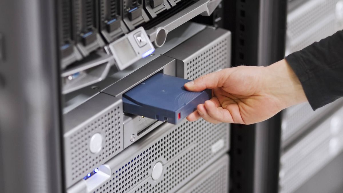 A close-up of a IT engineer / technician insert a backup tape in a backup robot in a rack.