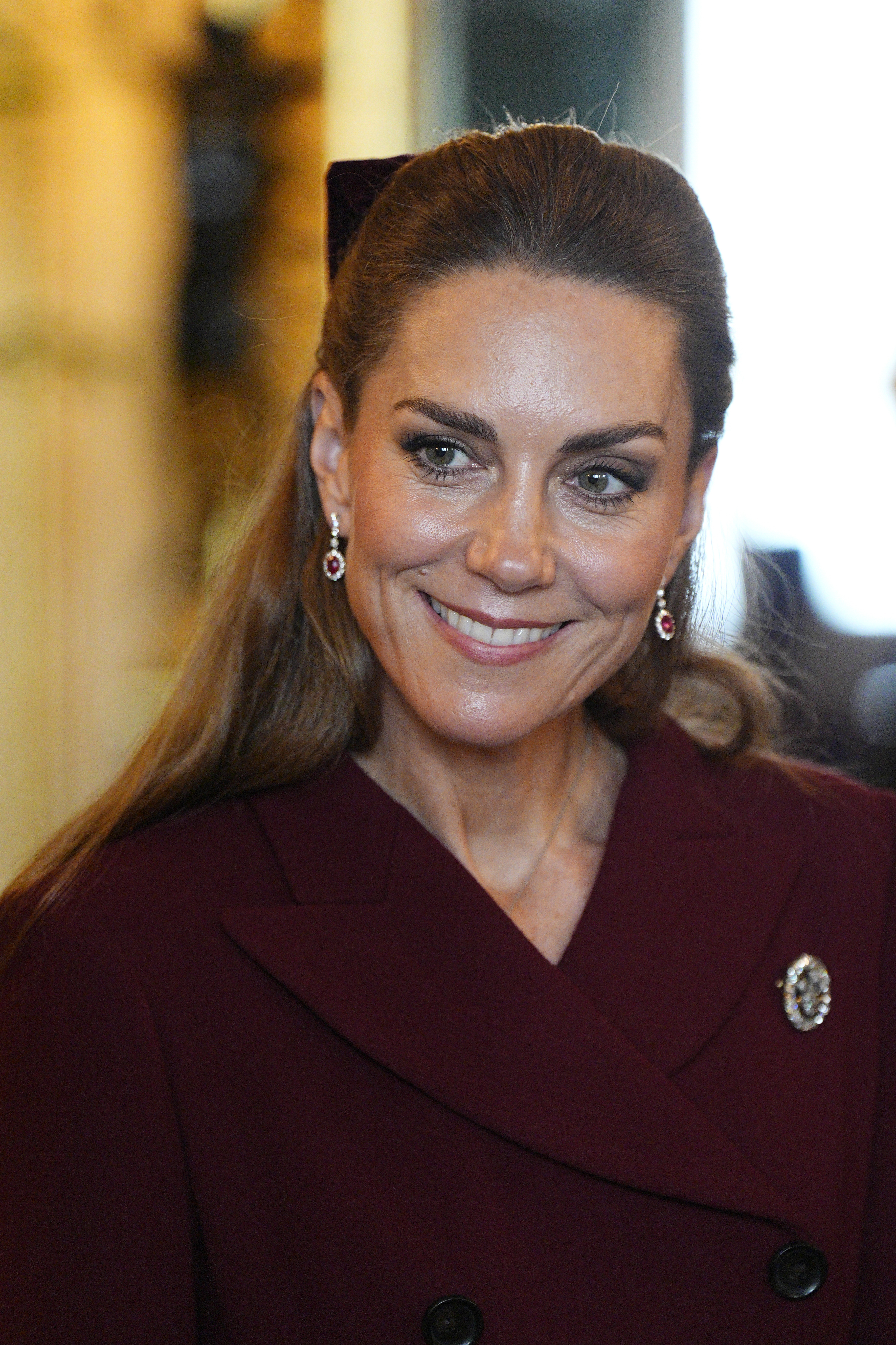 Kate Middleton wearing a burgundy coat and ruby earrings smiling