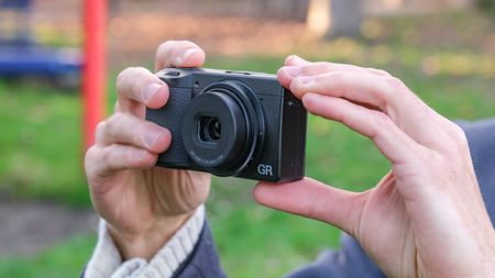 Ricoh GR IV compact camera held in a pair of hands