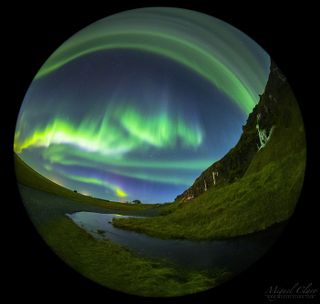 A full-dome, time-lapse image captured with a circular fisheye lens features a northern lights show above the cliffs of Seljalandsfoss, Iceland.
