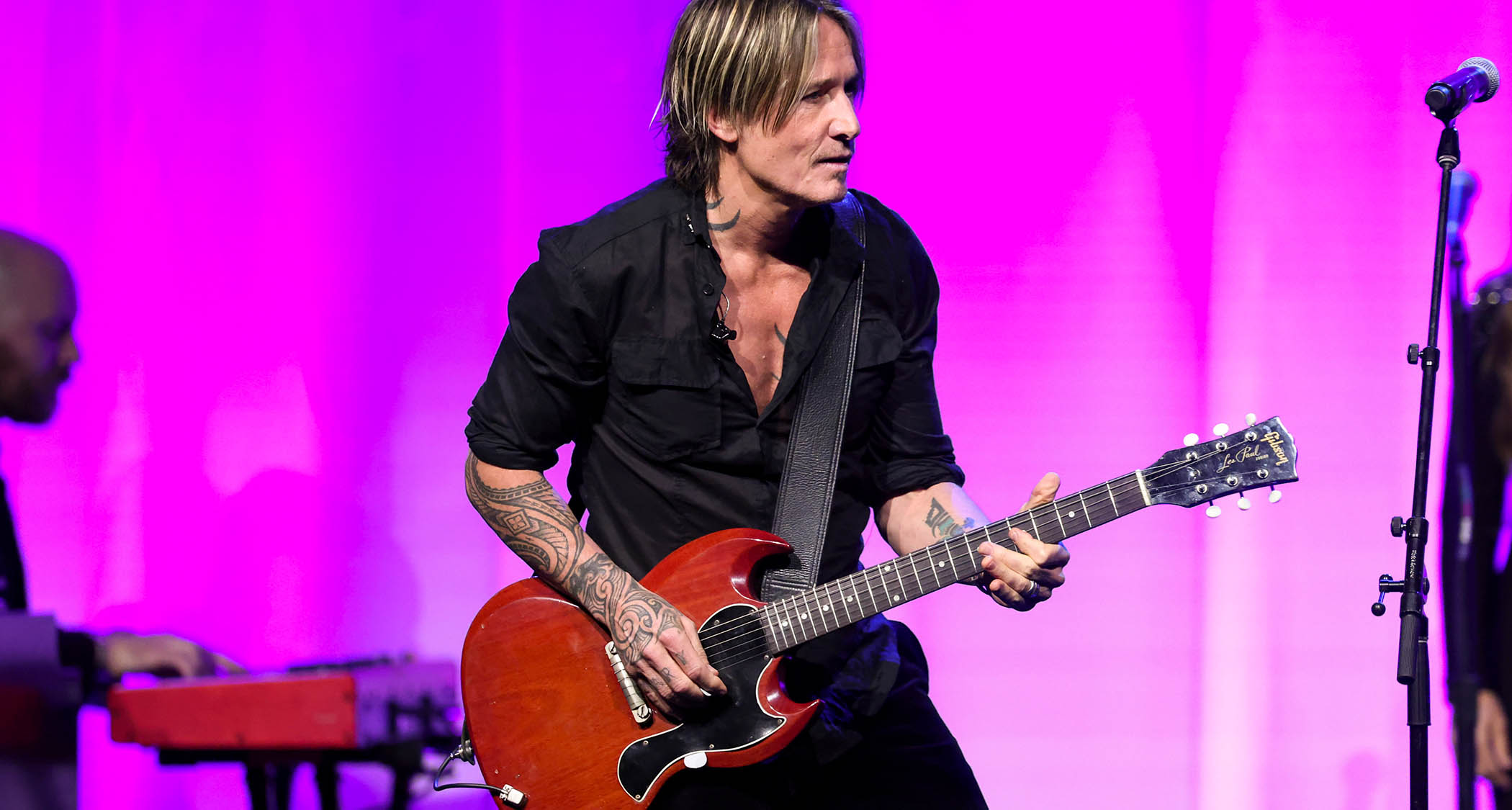 Keith Urban plays a cherry red Gibson SG against a pink background.