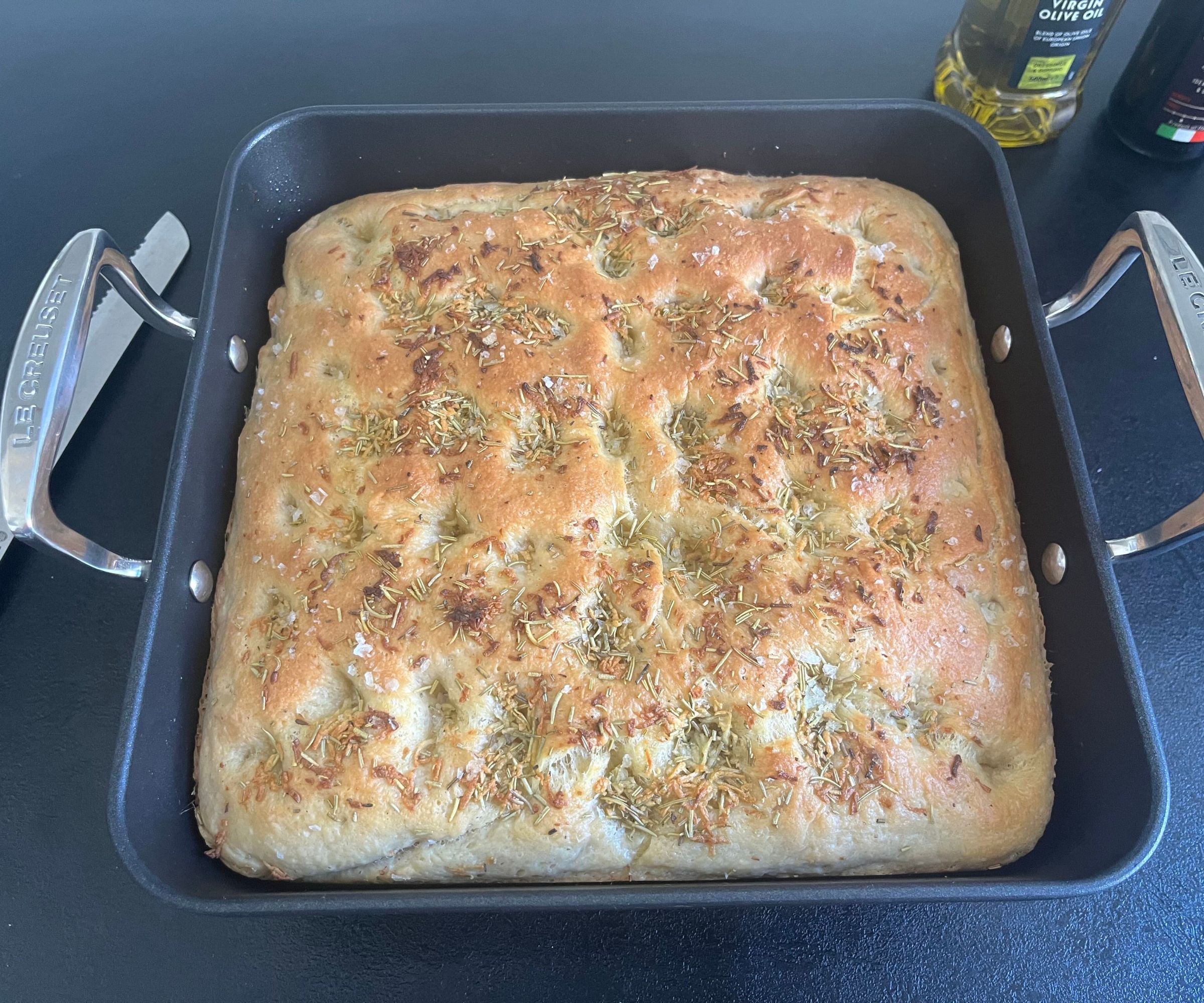 A fresh baked focaccia bread inside a black baking tray