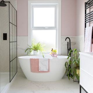 Bathroom with pink walls, white freestanding bath and plants