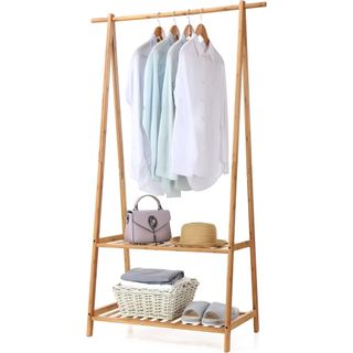 A bamboo clothing rail with hanging shirts, a handbag, hat, white wicker basket and grey slippers