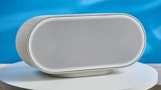 the denon home 600 home speaker in stone color photographed against the blue tom's guide background