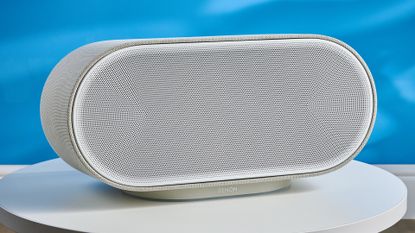 the denon home 600 home speaker in stone color photographed against the blue tom's guide background
