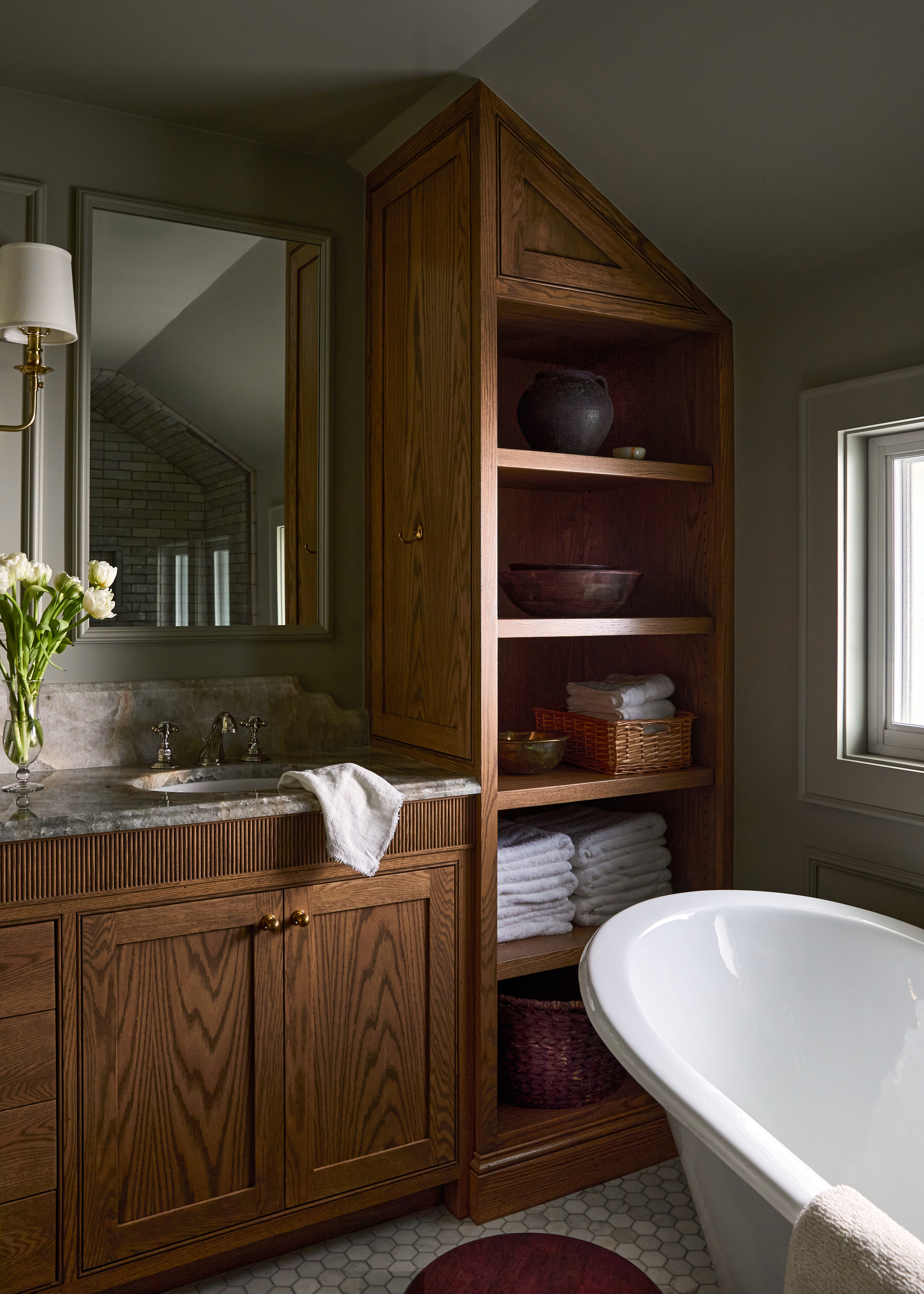 Image of a small bathroom with timber cabinetry and walls painted in a sage green color. There is a tub in view and gray marble countertops.