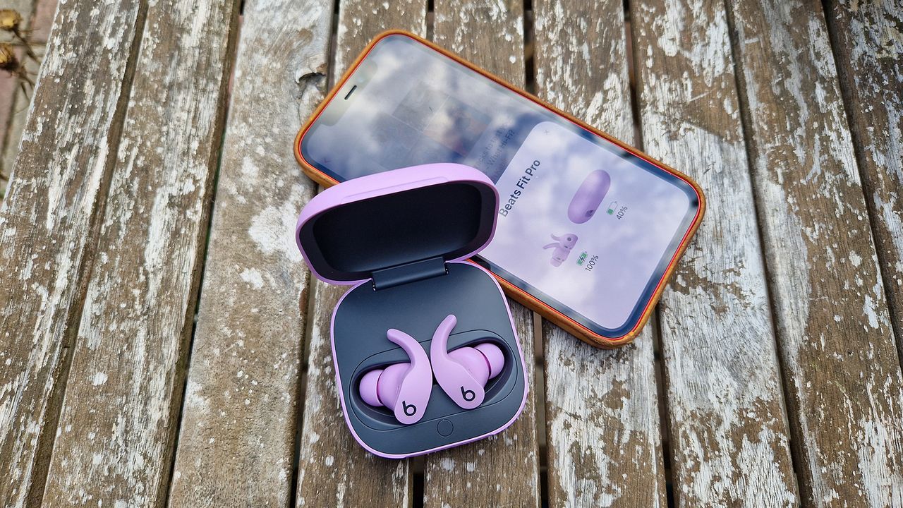 A pair of Beats Fit Pro in an open case with a smartphone.