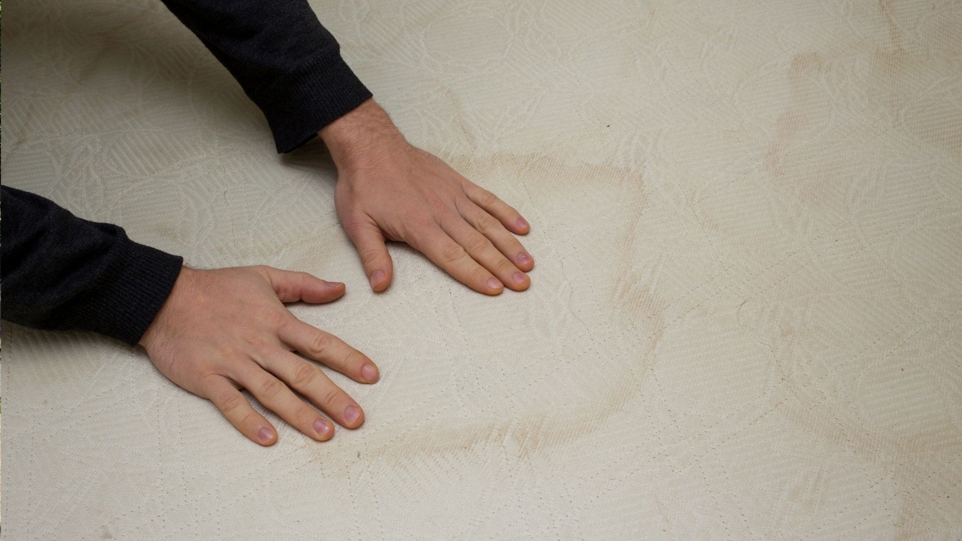 The image shows a person placing their hands on a sweat stained mattress