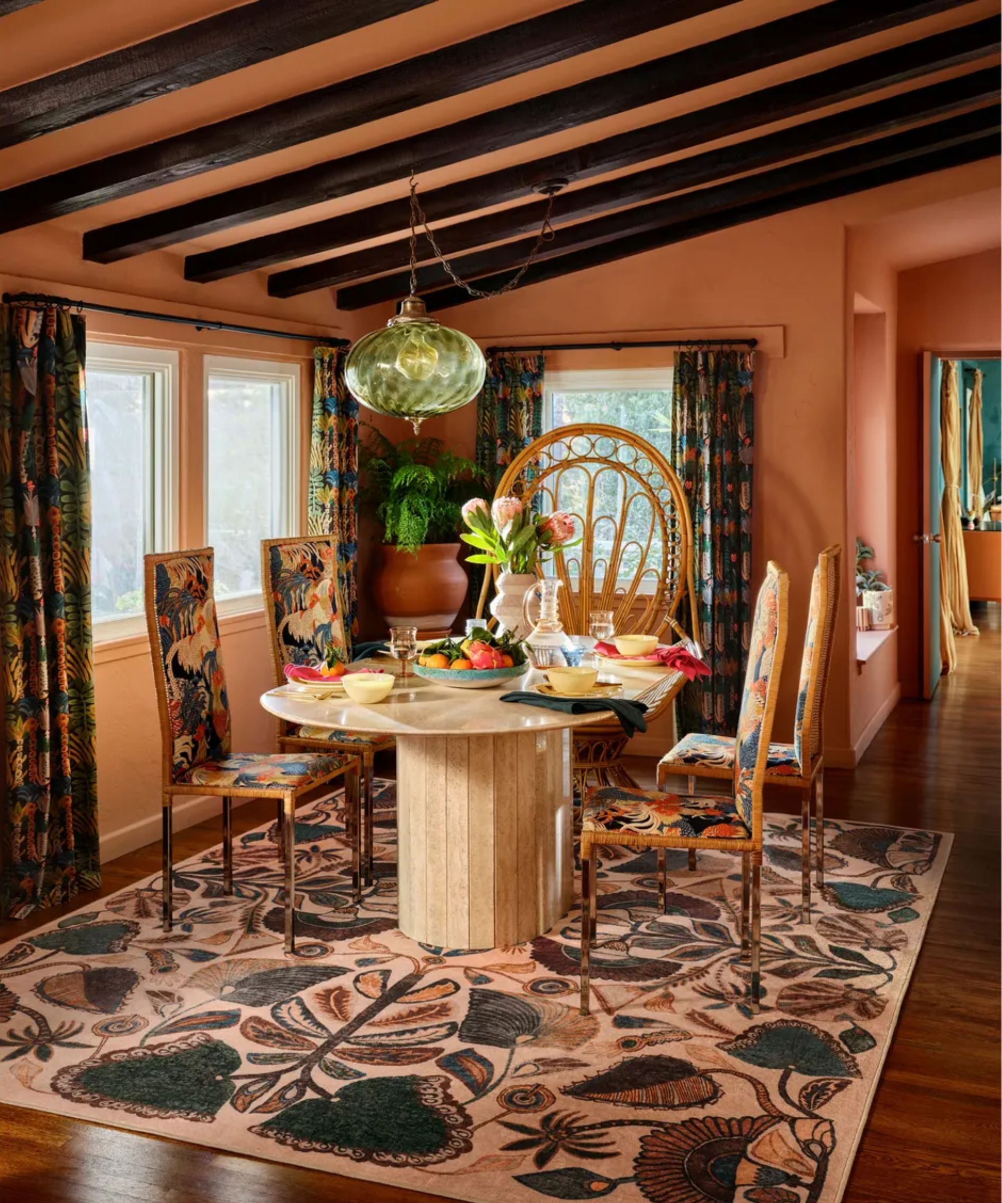 Maximalist dining room with oval wooden dining table, upholstered patterned chairs, rectangular patterned rug, terractotta painted walls