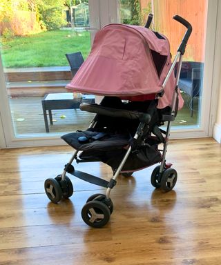 Pink and black stroller indoors on a wooden floor and with a glass door behind overlooking a yard