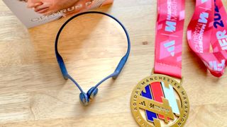 a photo of the Shokz OpenRun Pro earphones next to writer Jessica's Adidas Manchester Marathon finisher medal